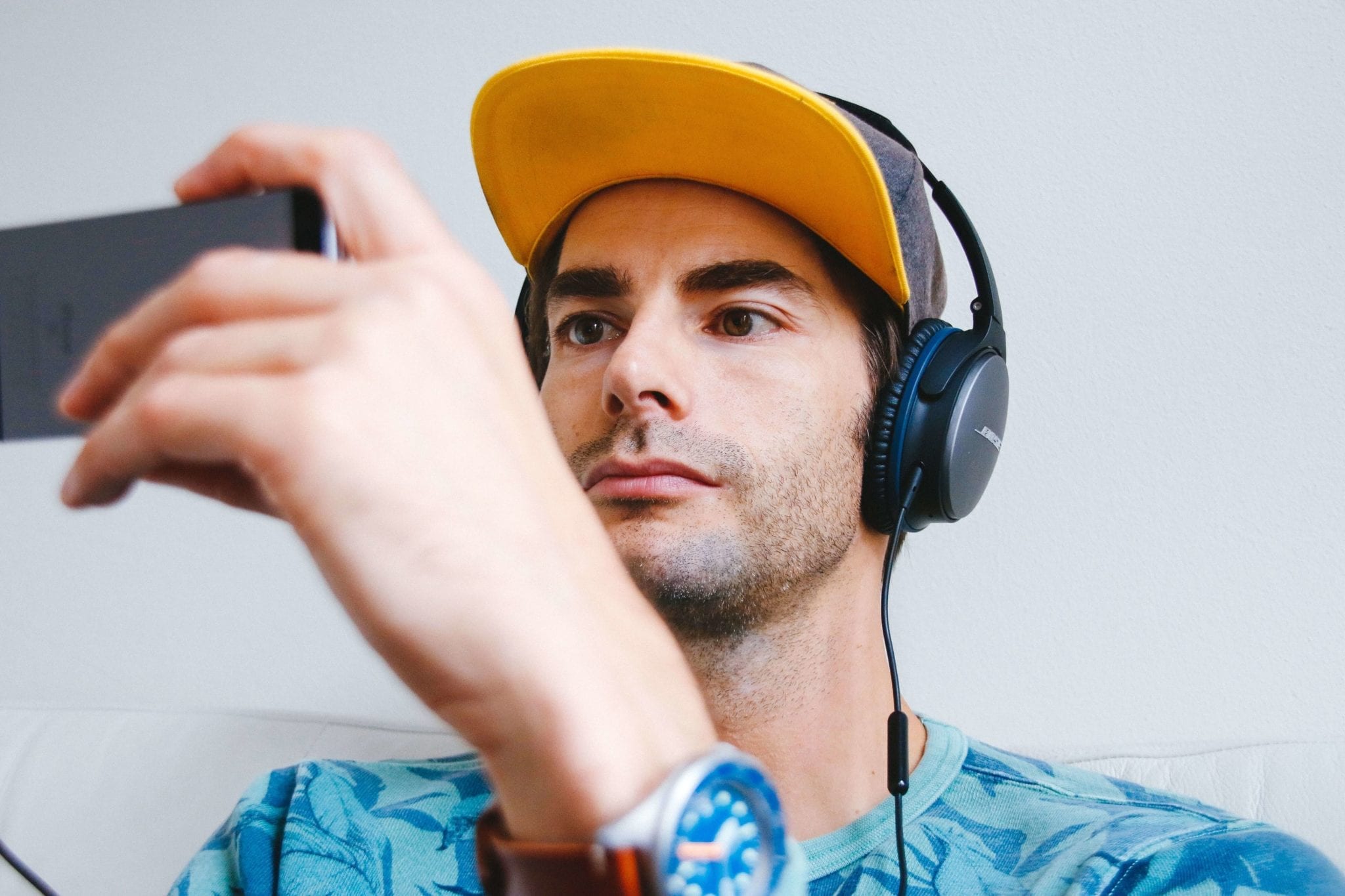 Ein junger Mann, der Kopfhörer trägt und Medien über ein Smartphone konsumiert